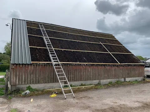 Overcladding in progress: new battens fixed over an old moss-covered cement-sheet barn roof, with the first grey profile sheets on at the verge