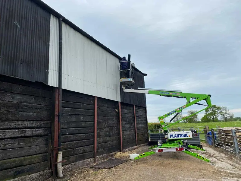 Operative on a cherry picker fixing new profiled cladding sheets to the upper wall of a steel-framed barn