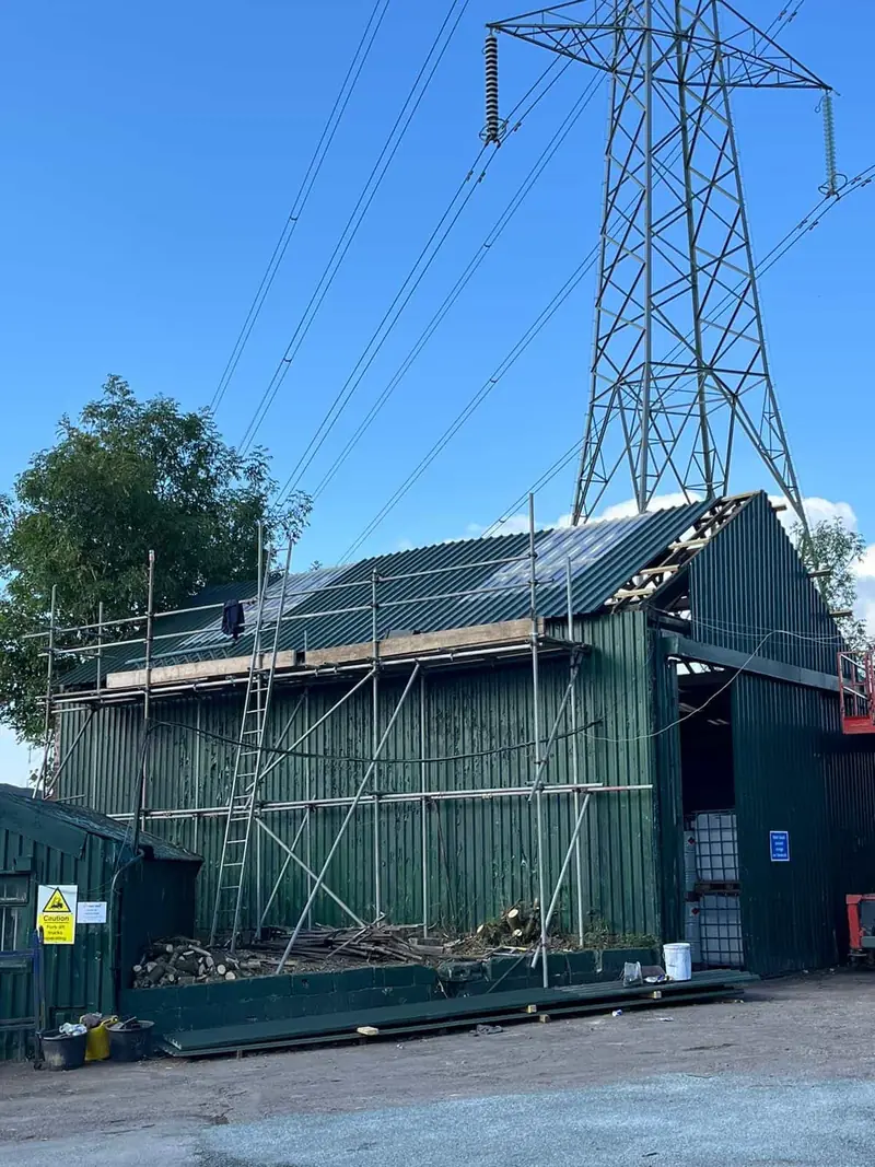 Scaffolding around a green steel-clad building during re-roofing with new profile sheets and rooflights